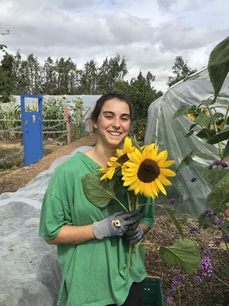 Maryam smiling, holding sunflowers on a farm